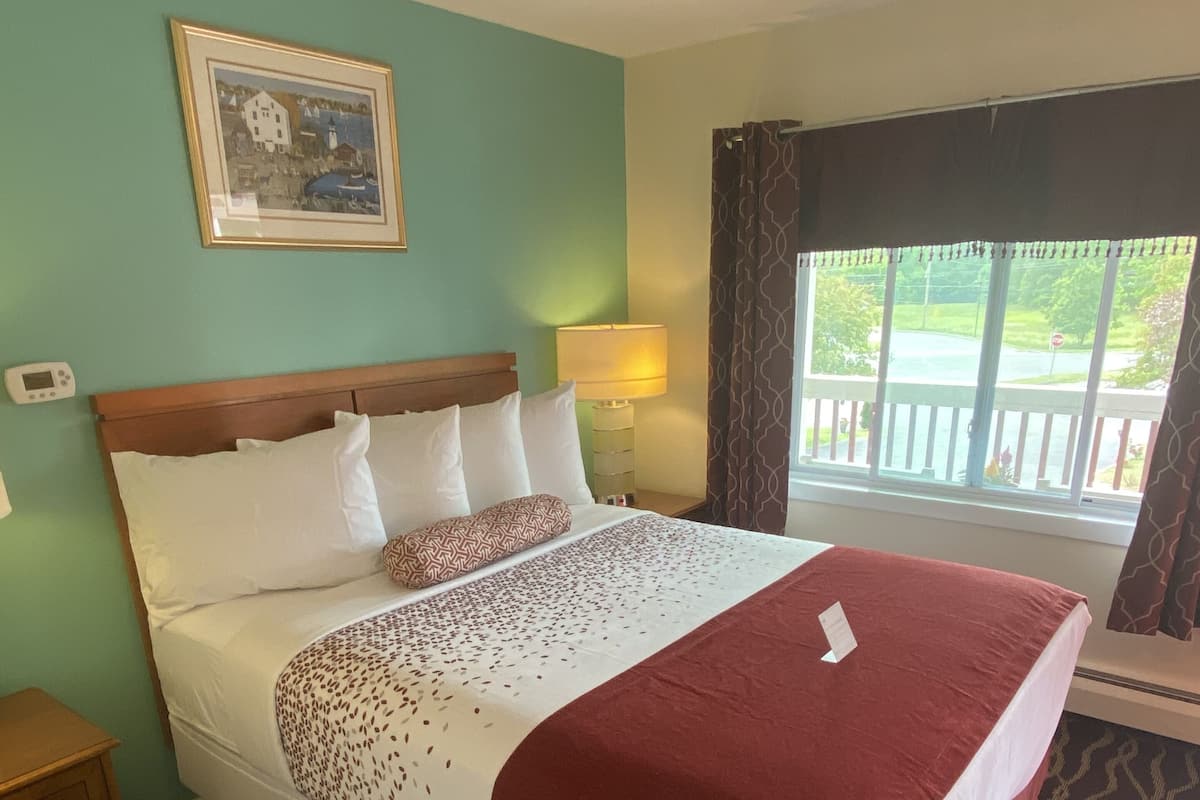 Une chambre d’hôtel avec un lit, une table de chevet, une lampe, une fenêtre avec des rideaux et un tableau au mur.