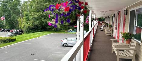 A covered outdoor area with a row of white benches and hanging flower baskets.