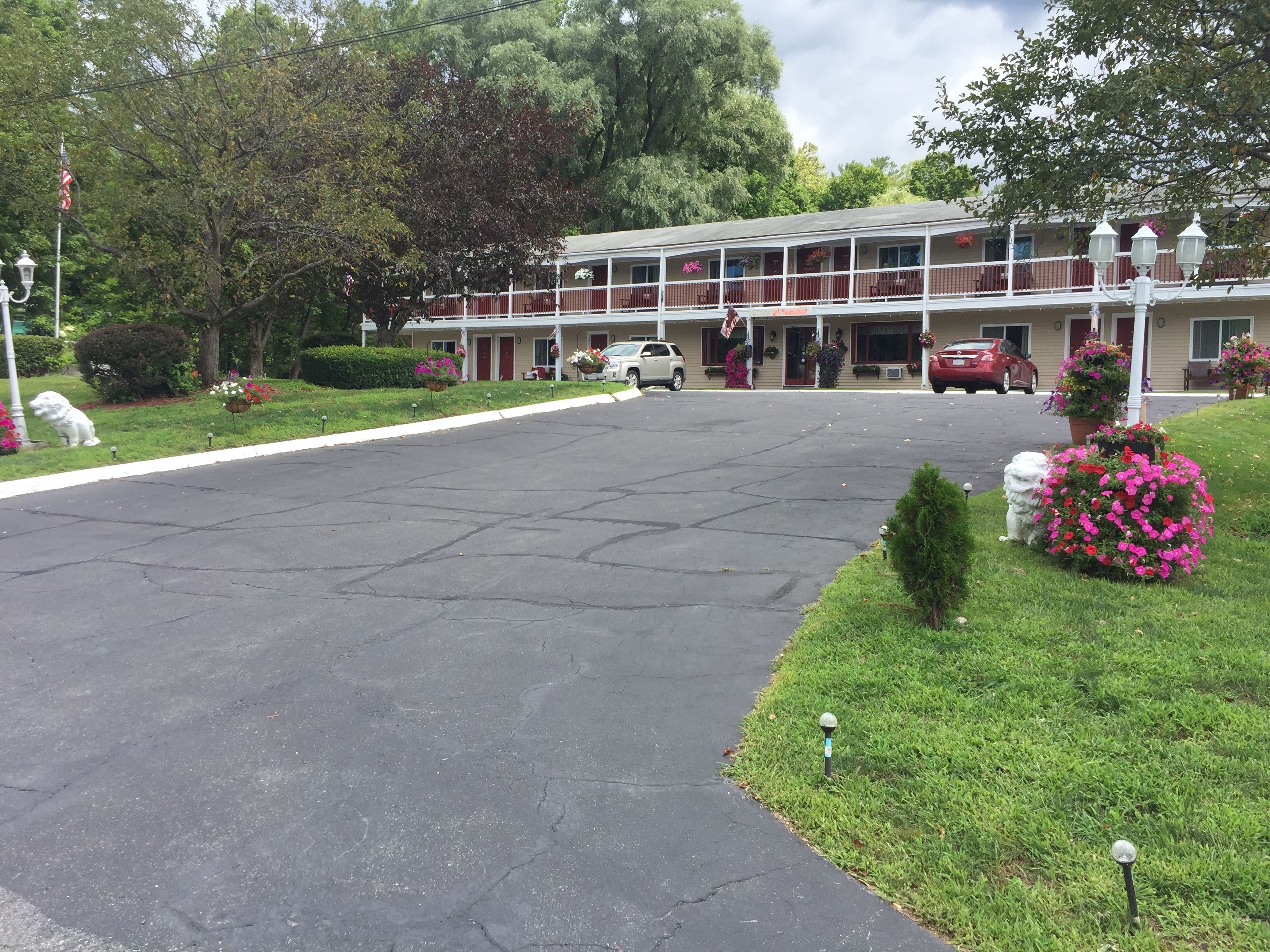 A motel with a two-story structure, a covered parking area, and a well-maintained lawn with flower beds.