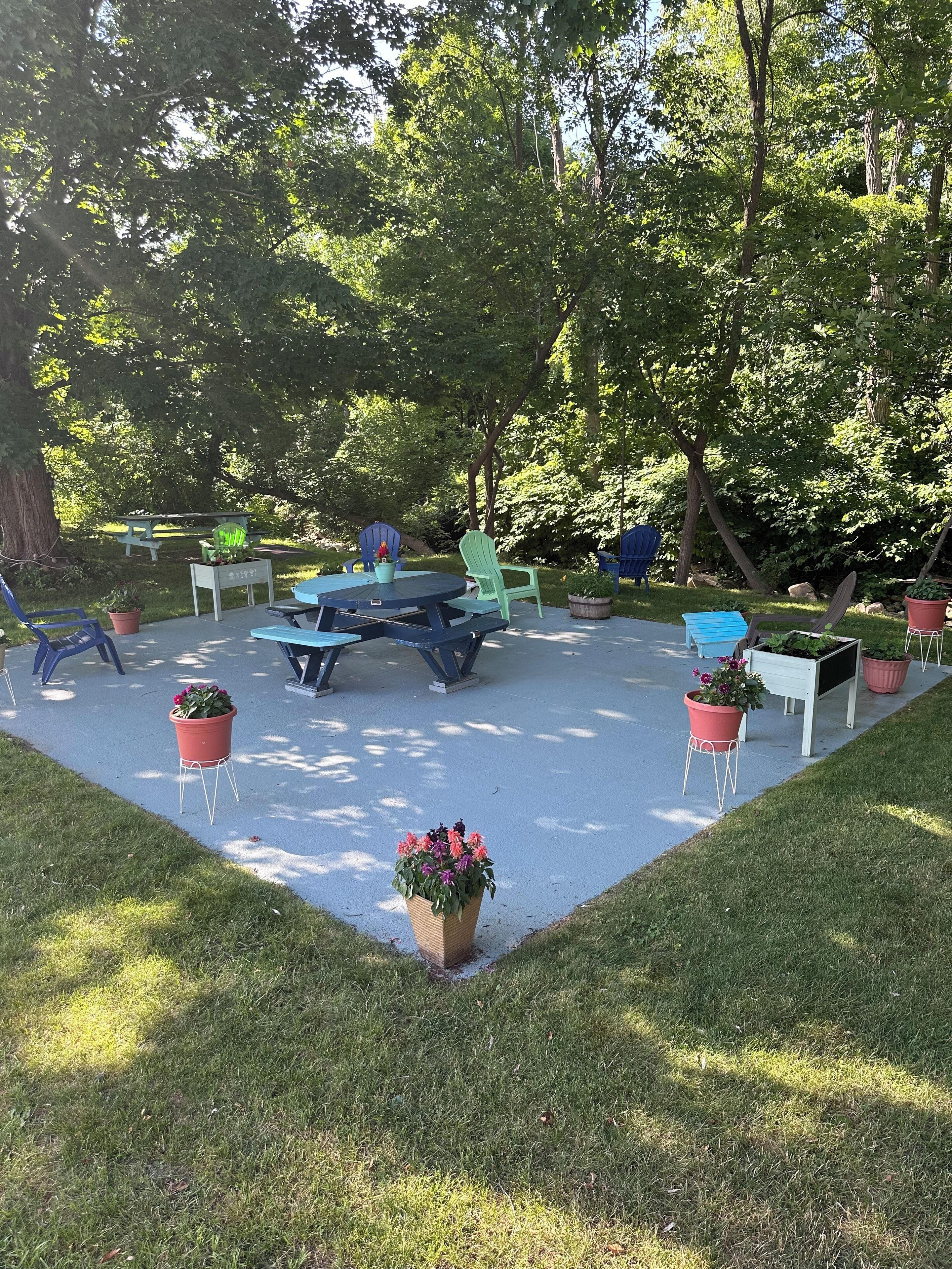 An outdoor seating area with tables and chairs, surrounded by greenery and trees.