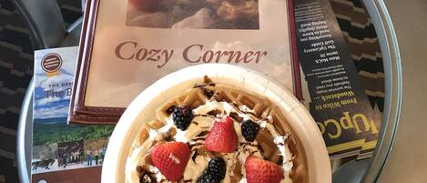 Un plato de postre con fresas y crema batida, un libro titulado 'Cozy Corner' y una revista sobre una mesa.