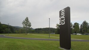 A sign with the word "CLARM" on a grassy field with a road and trees in the background. - Cozy Corner Motel (Williamstown)