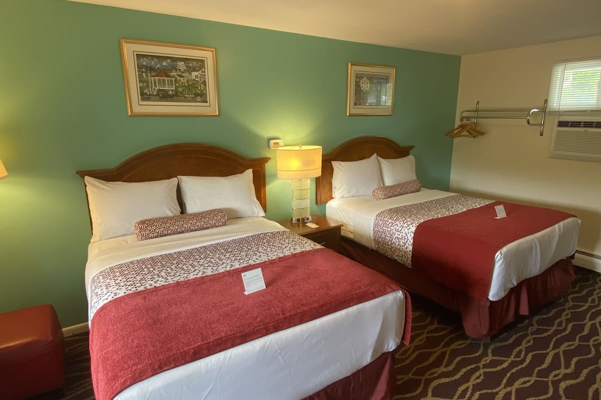 Une chambre d’hôtel avec deux lits, chacun recouvert d’une couverture rouge et agrémenté d’oreillers blancs, une table de chevet avec une lampe et un tableau encadré au mur.