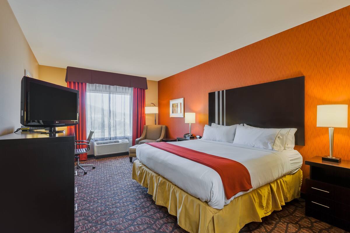 A hotel room with a large bed, a desk with a TV, a chair, a desk lamp, and a picture on the wall.