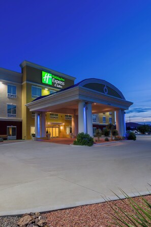 A Holiday Inn Express & Suites building with a modern design, featuring a large entrance and a clear sky in the background.