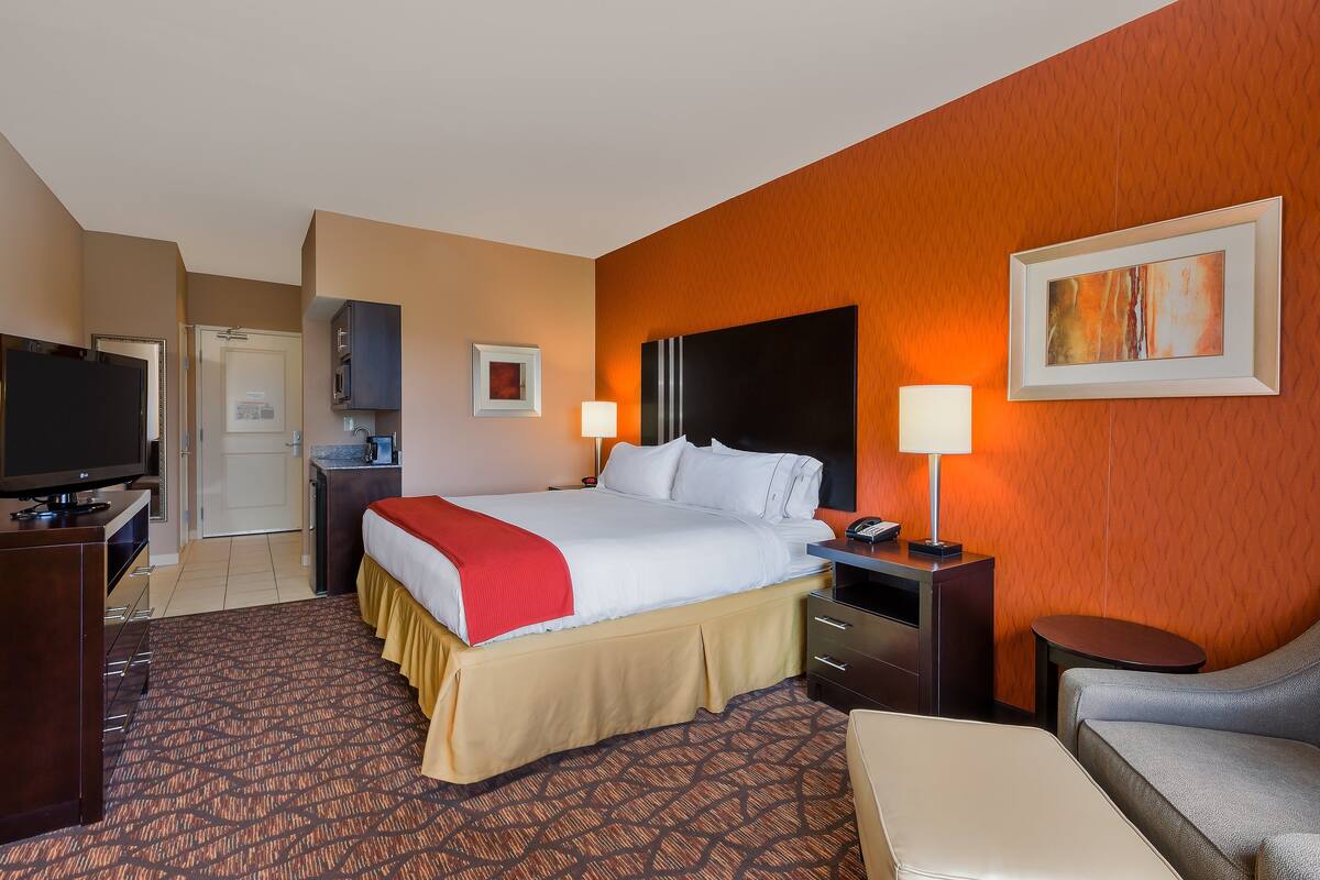 A hotel room with a bed, a TV, a desk, a chair, and a painting on the wall.
