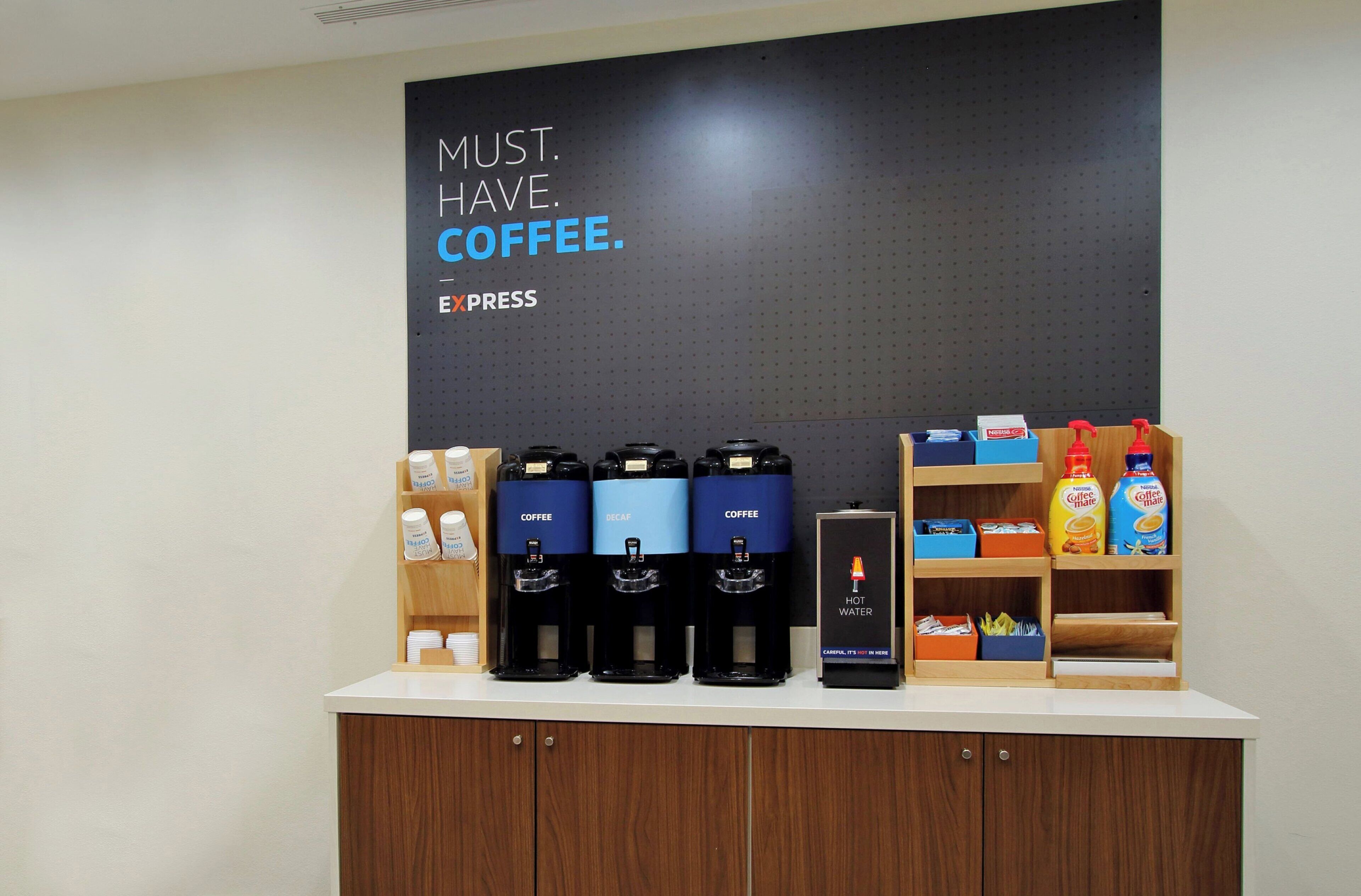Una estación de café con varios dispensadores de café, un dispensador de agua caliente y un letrero que dice 'MUST. HAVE. COFFEE'.
