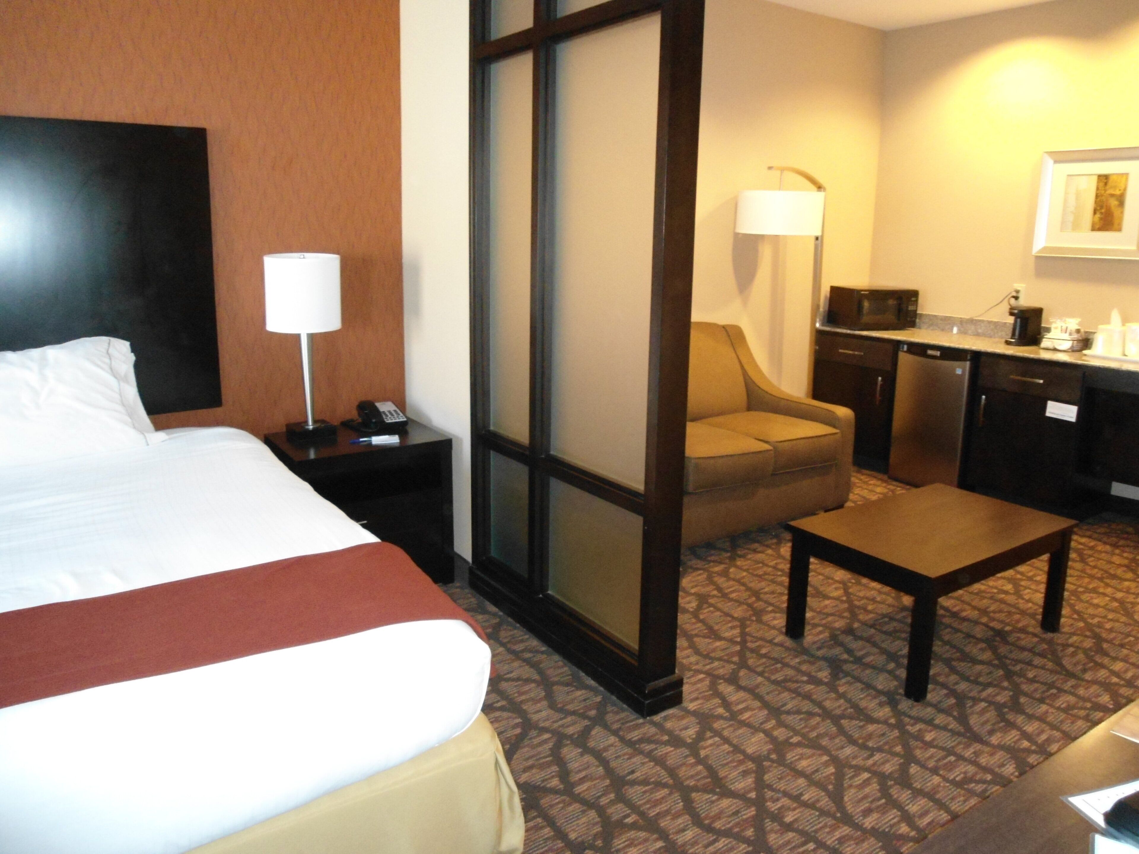 A hotel room with a bed, a desk, a chair, a small table, a microwave, and a coffee maker.