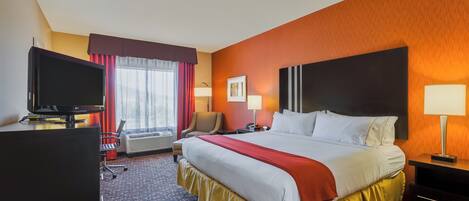 A hotel room with a large bed, a desk with a television, a chair, and a window with curtains.