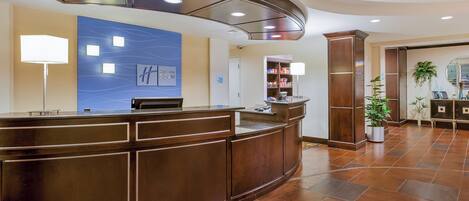 A hotel reception area with a curved reception desk, a blue wall with a Holiday Inn Express sign, a check-in counter, and a plant in the corner.