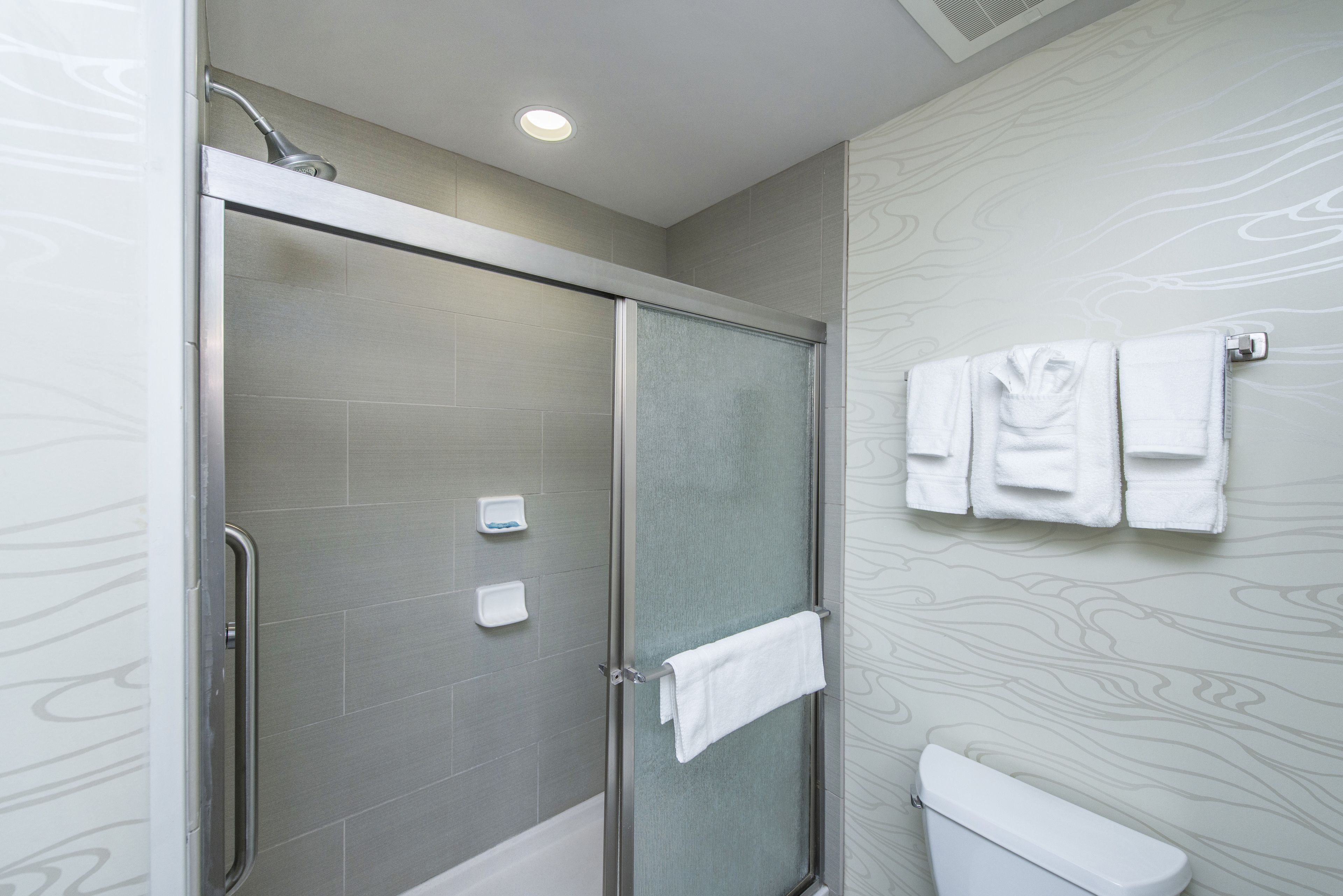 Un baño moderno con ducha de vidrio, inodoro y toallero con varias toallas.