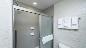 Un baño moderno con ducha de vidrio, inodoro y toallero con varias toallas.