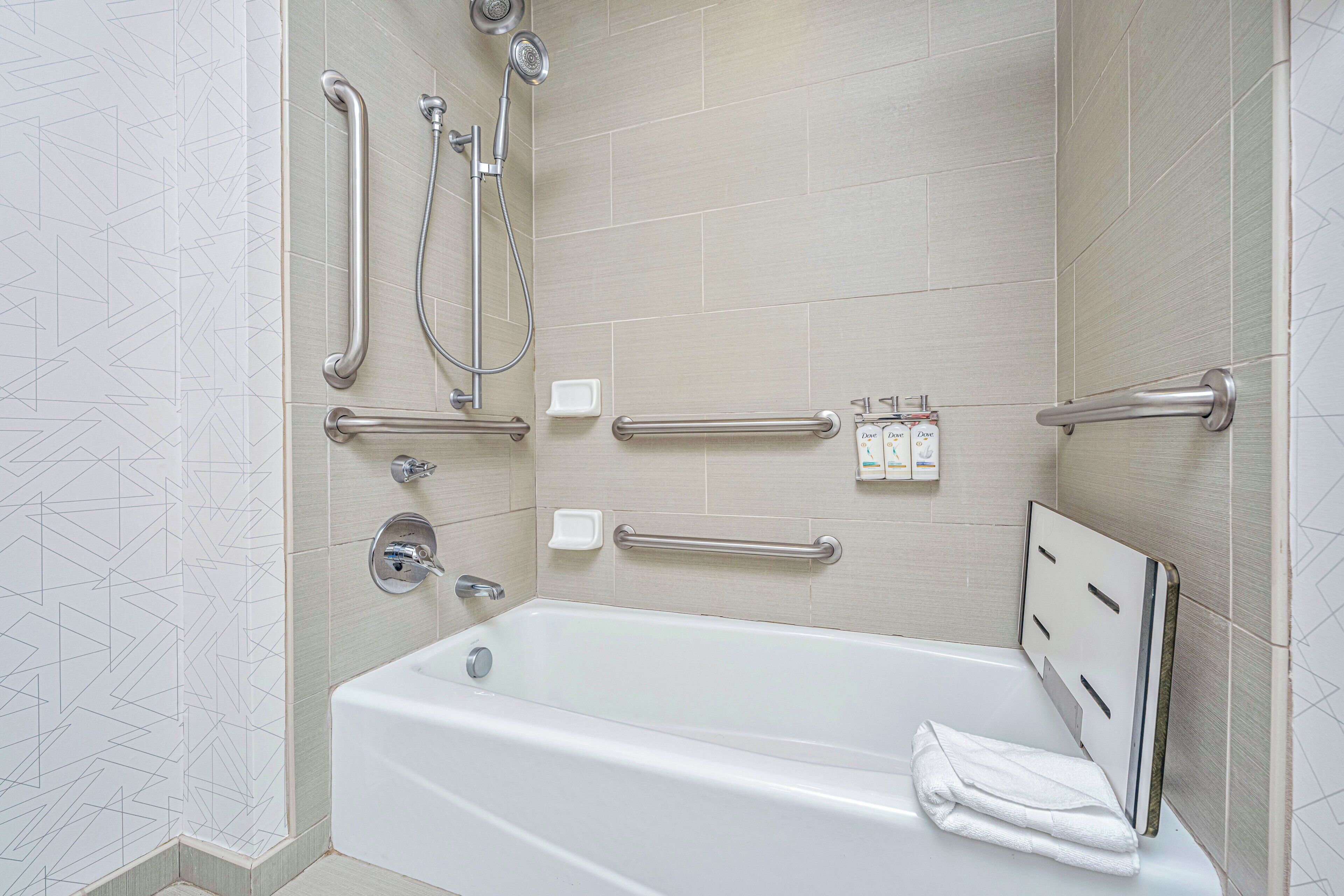 A modern bathroom with a bathtub, grab bars, a handheld showerhead, and a towel rack.