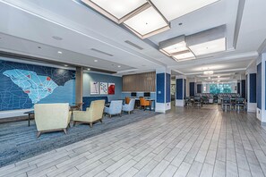 A spacious lobby with a modern design, featuring a large seating area with multiple chairs and tables, a large wall mural, and a high ceiling with skylights. - Holiday Inn Express & Suites Charleston Arpt-Conv Ctr Area (North Charleston)