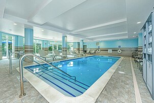Una piscina interior con agua azul cristalina, rodeada de sillones de descanso y un suelo de baldosas.