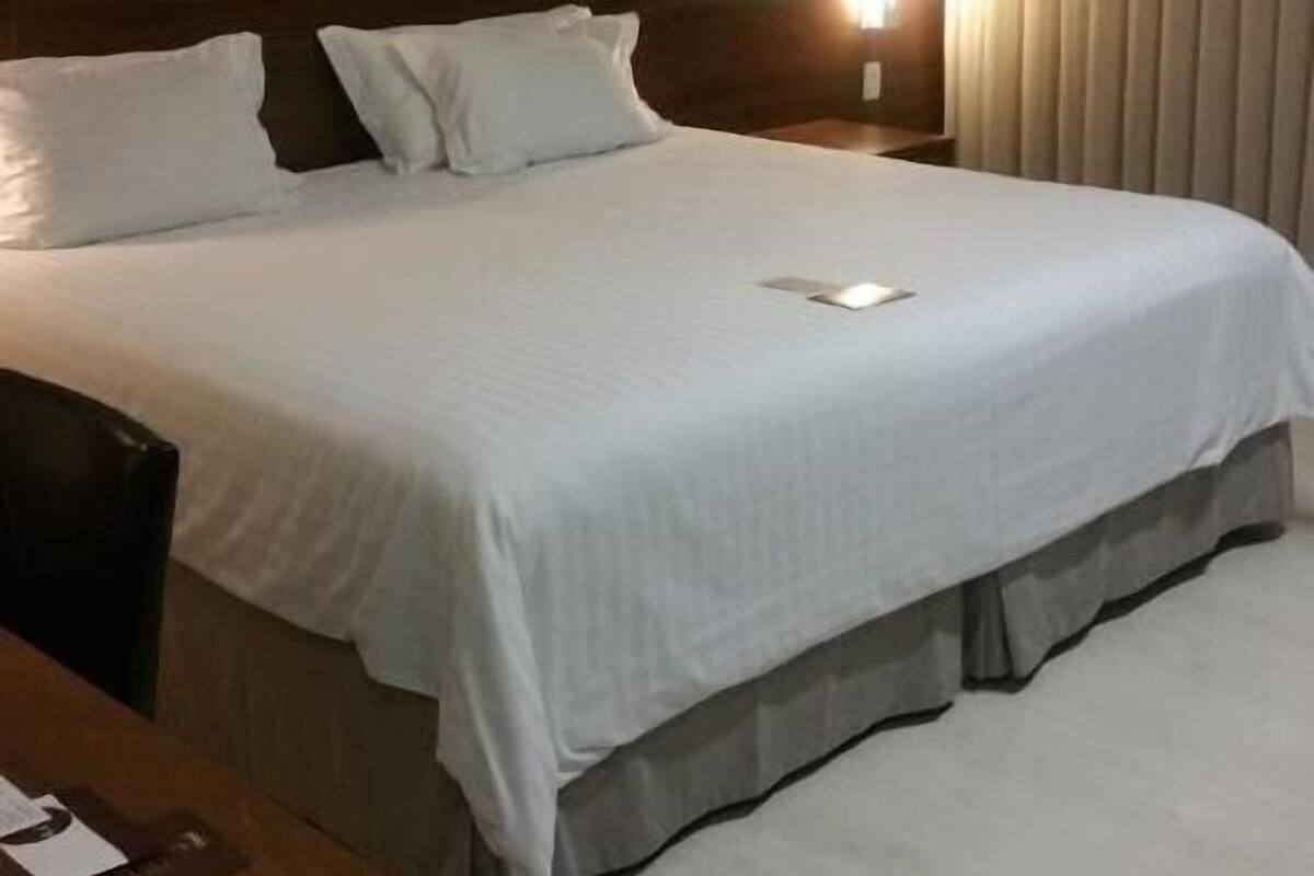 Una habitación de hotel con una cama grande, una mesita de noche y una lámpara.