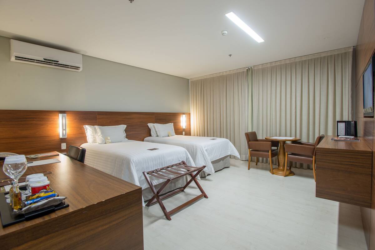 Una habitación de hotel con dos camas, un escritorio, una silla, una mesita y un equipo de aire acondicionado.