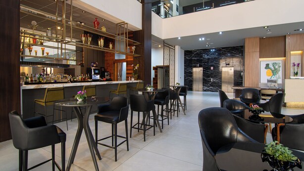 A modern bar area with a high ceiling, multiple seating options, and a visible elevator. - Hotel Gran Odara (Cuiabá)