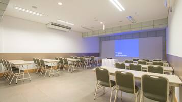 Una sala conferenze con diversi tavoli e sedie, uno schermo per proiettore e una lavagna.