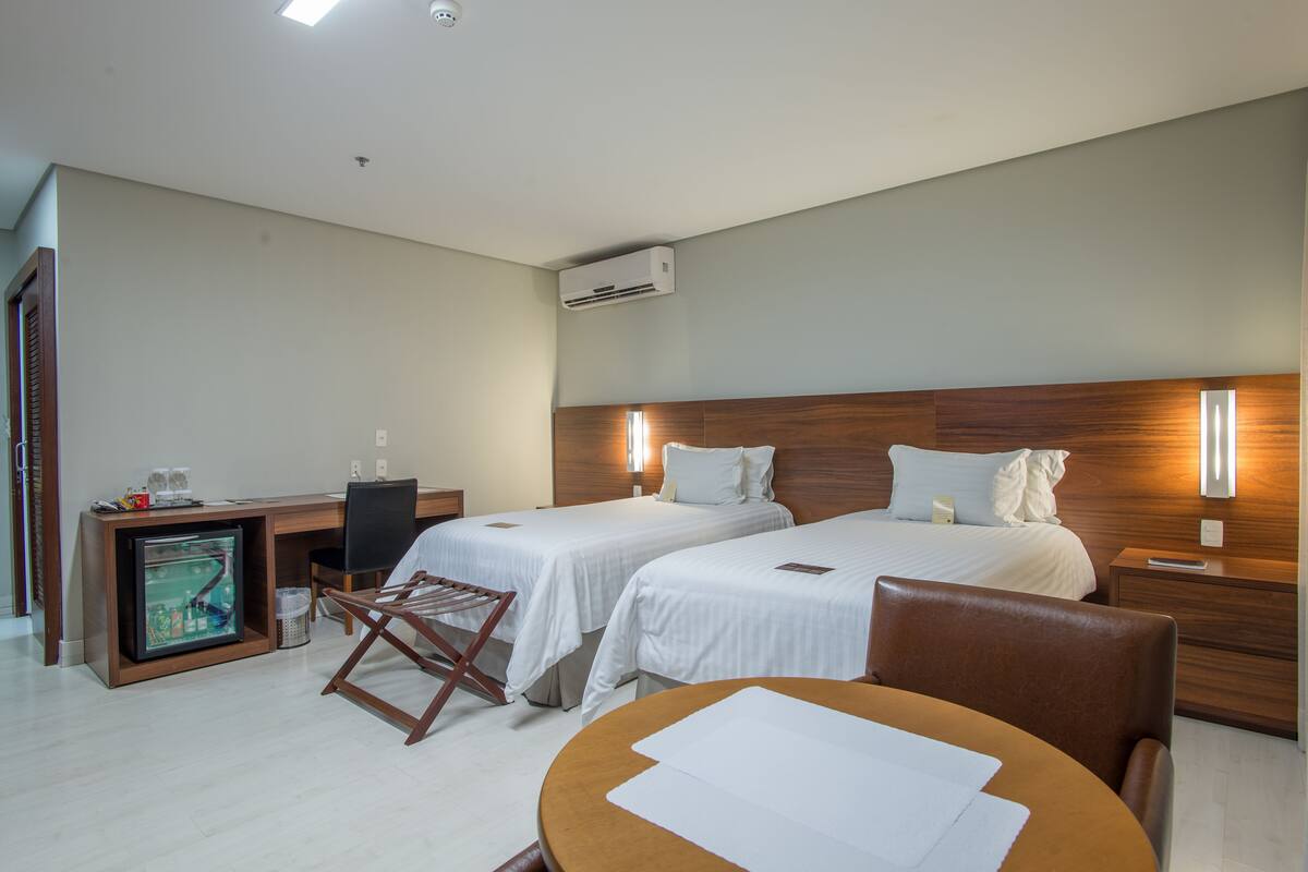 Habitación de hotel con dos camas, un escritorio, una silla, una mesa y un televisor.