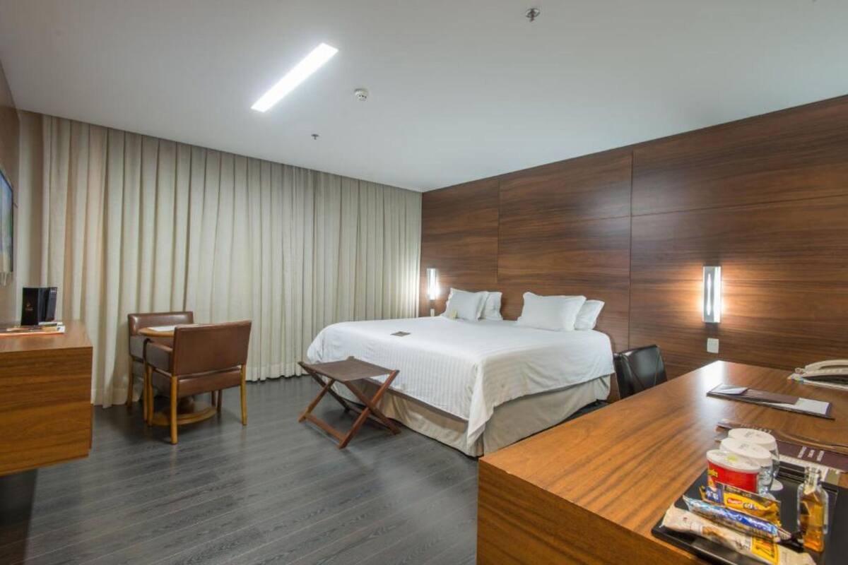 Una habitación de hotel moderna con una cama grande, un escritorio con silla, una mesita pequeña y un minibar.