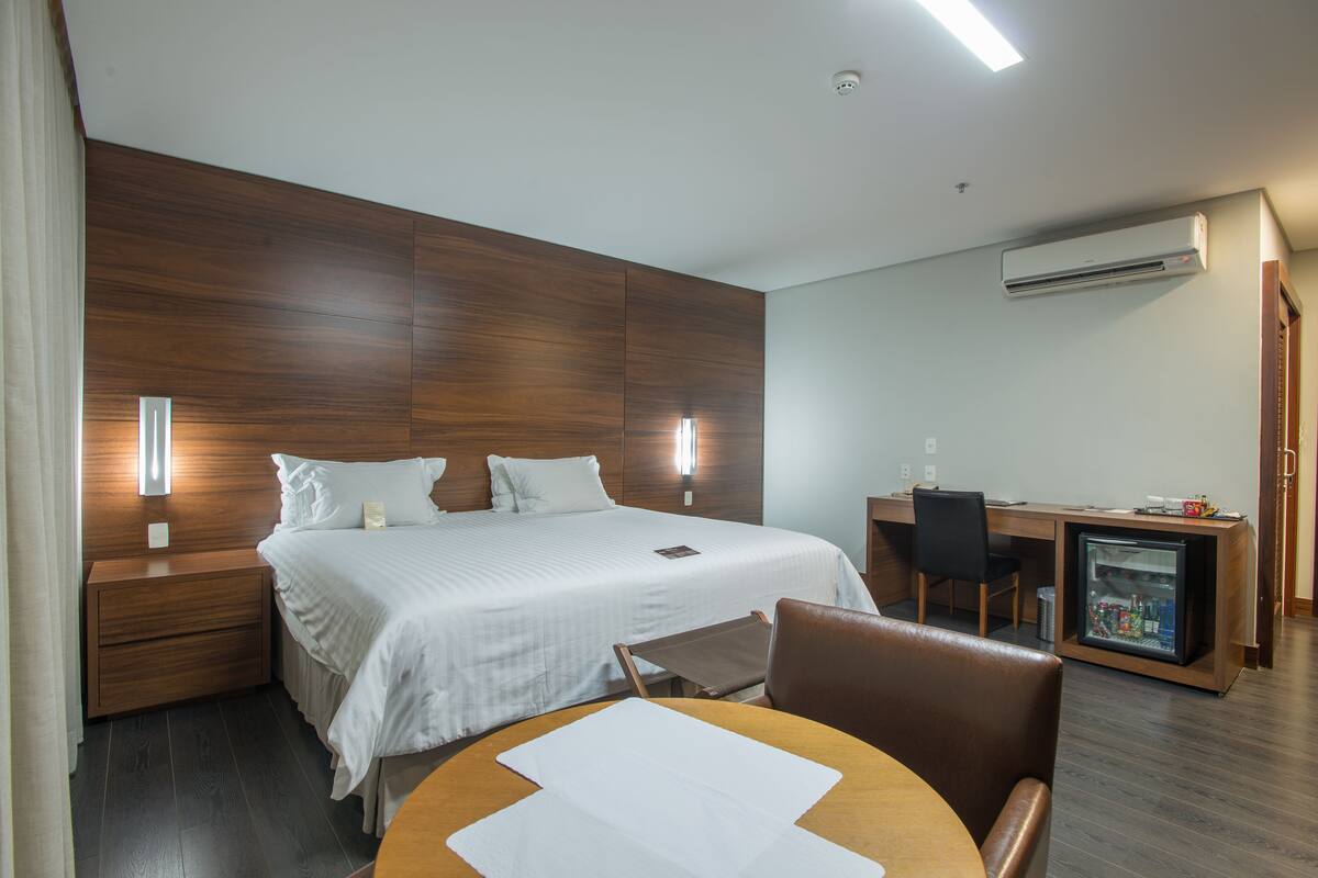 Una habitación de hotel con cama, mesitas de noche, escritorio, silla y minibar.