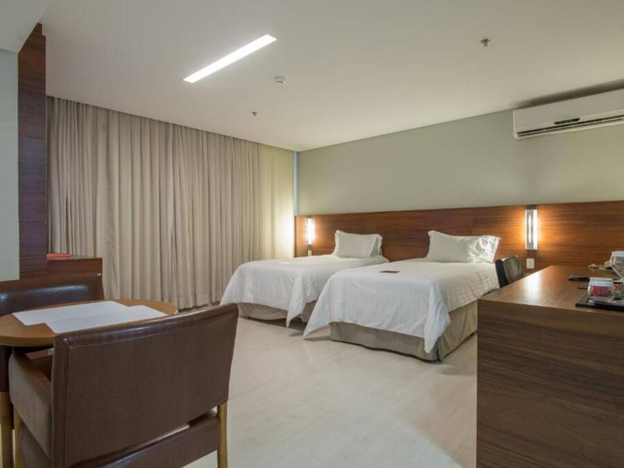 A hotel room with two beds, a desk, a chair, and an air conditioning unit.