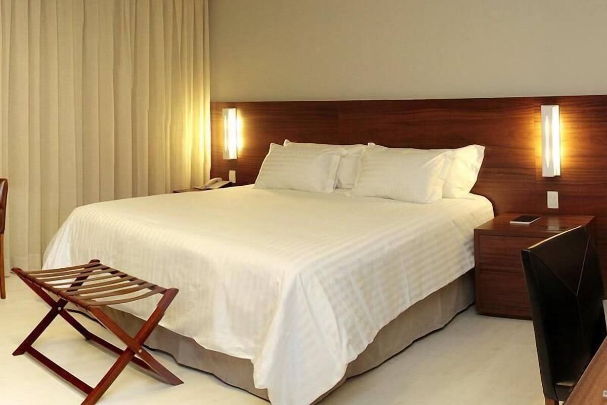 Habitación de hotel con una cama grande, mesitas de noche, una silla y un televisor de pantalla plana.