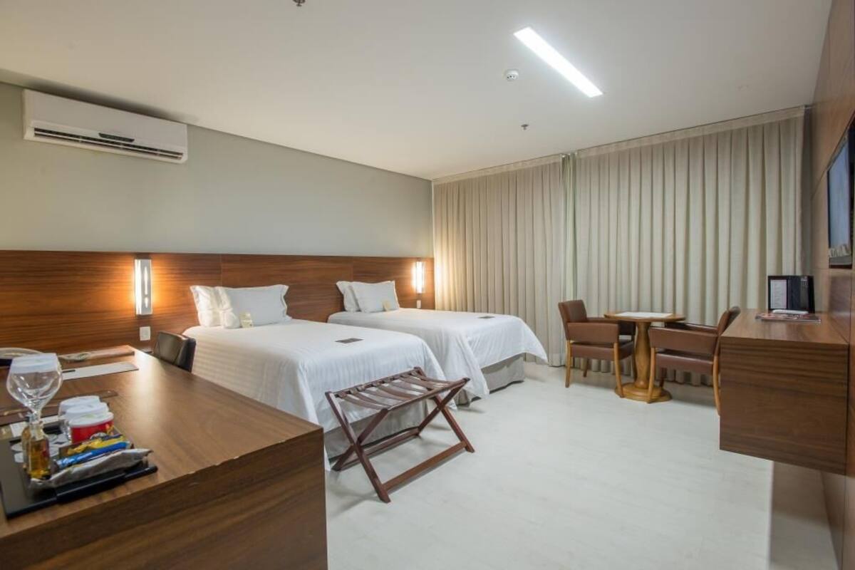 Habitación de hotel con dos camas, un escritorio, una silla, una mesita y un equipo de aire acondicionado.