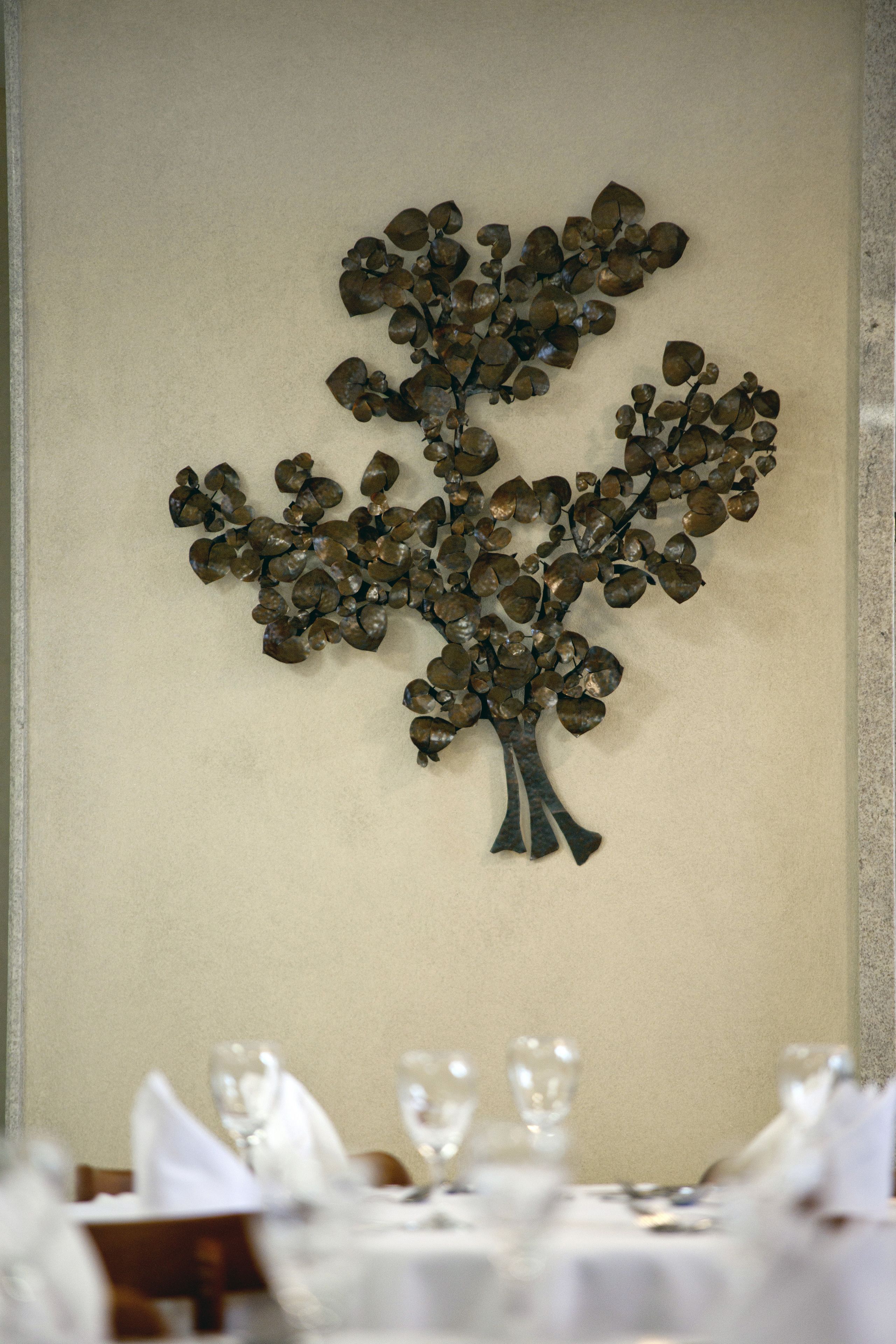A dining table with a metal tree decoration on the wall behind it.