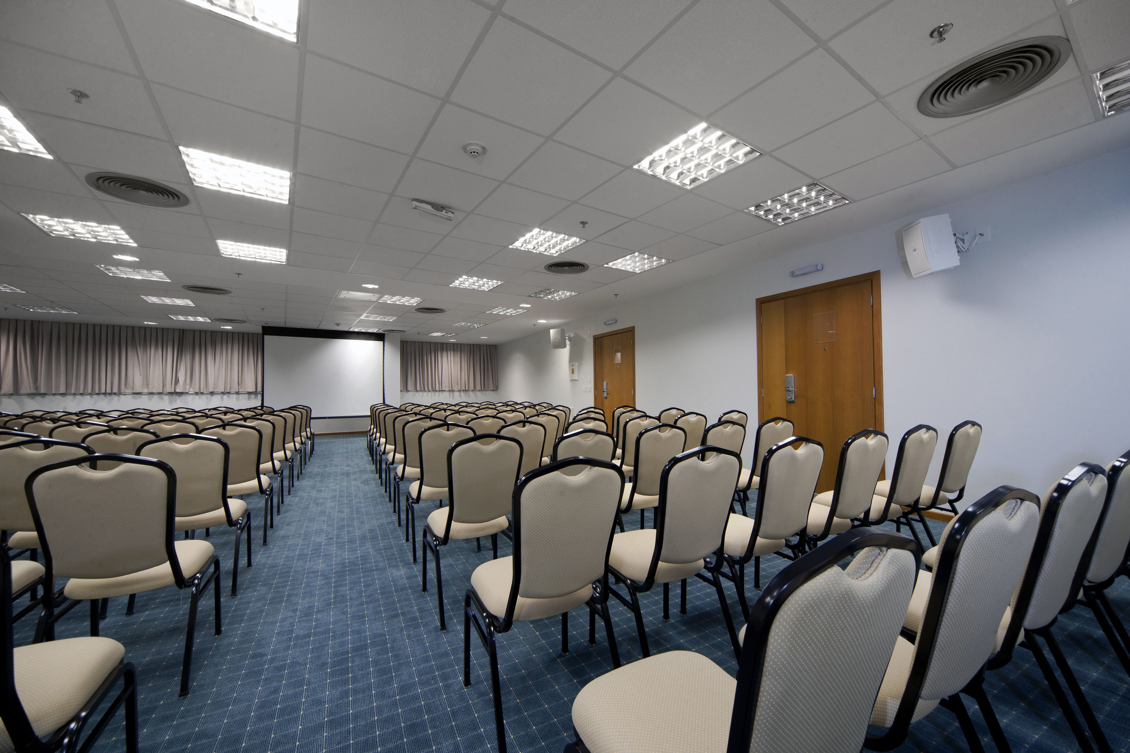 A conference room with rows of chairs, a projector screen, and a door.