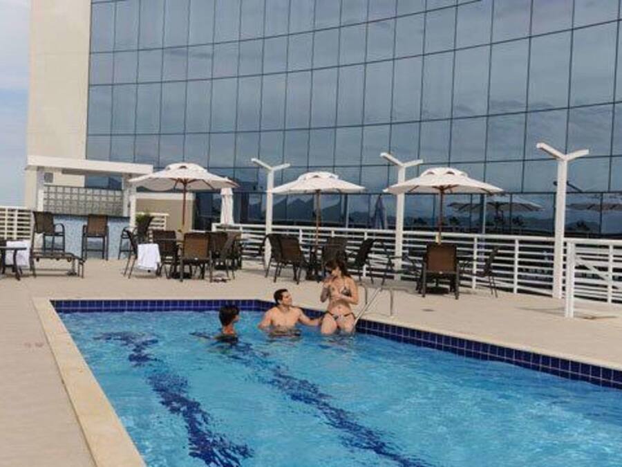Una piscina con sillas de descanso y sombrillas, rodeada por un edificio moderno con grandes ventanales.