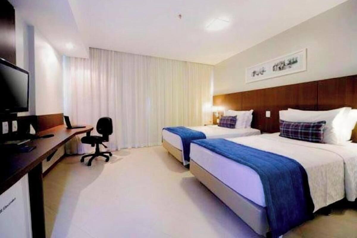 A hotel room with two beds, a desk with a computer, a TV, and a chair.