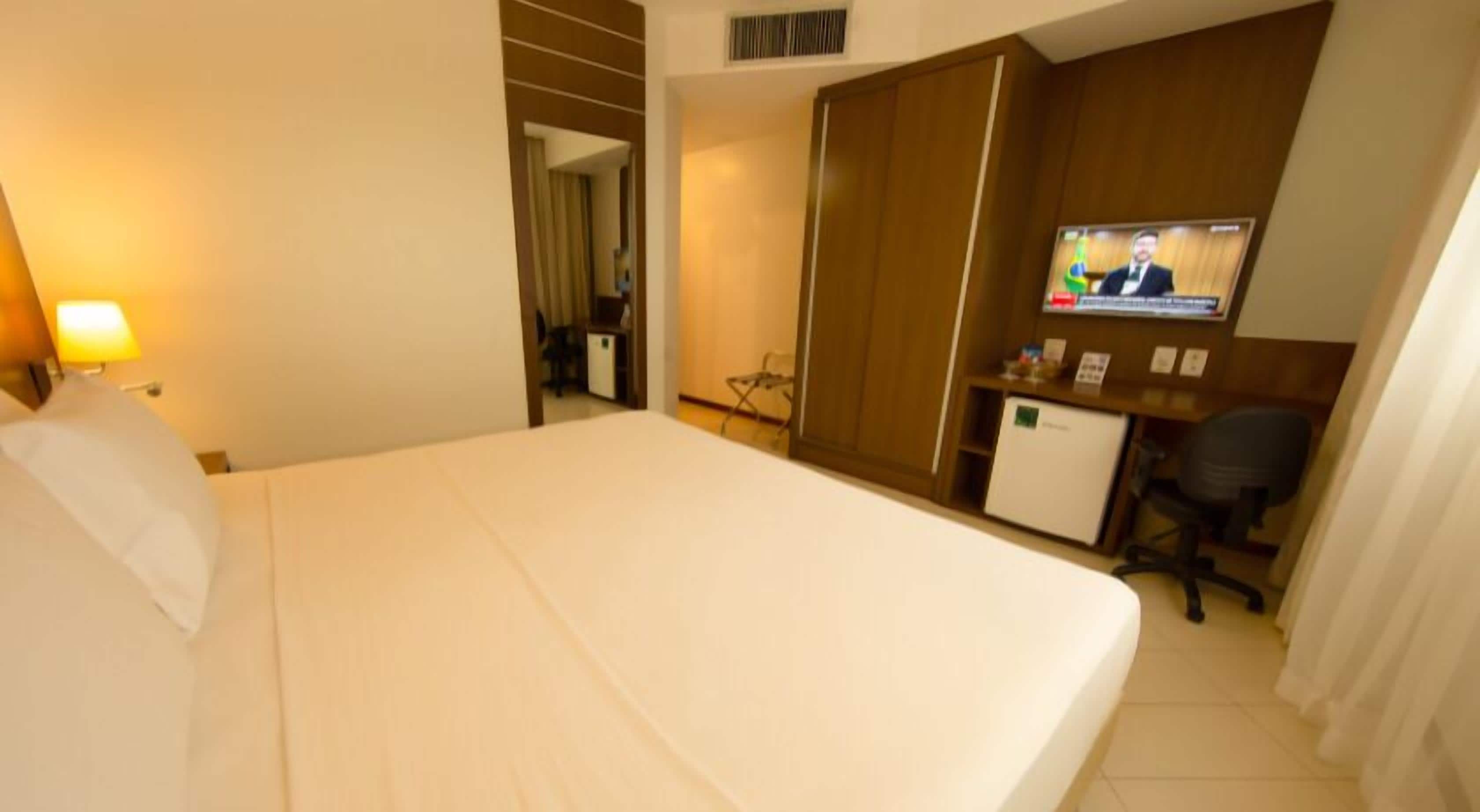 A hotel room with a bed, a desk with a computer, a TV, and a small refrigerator.