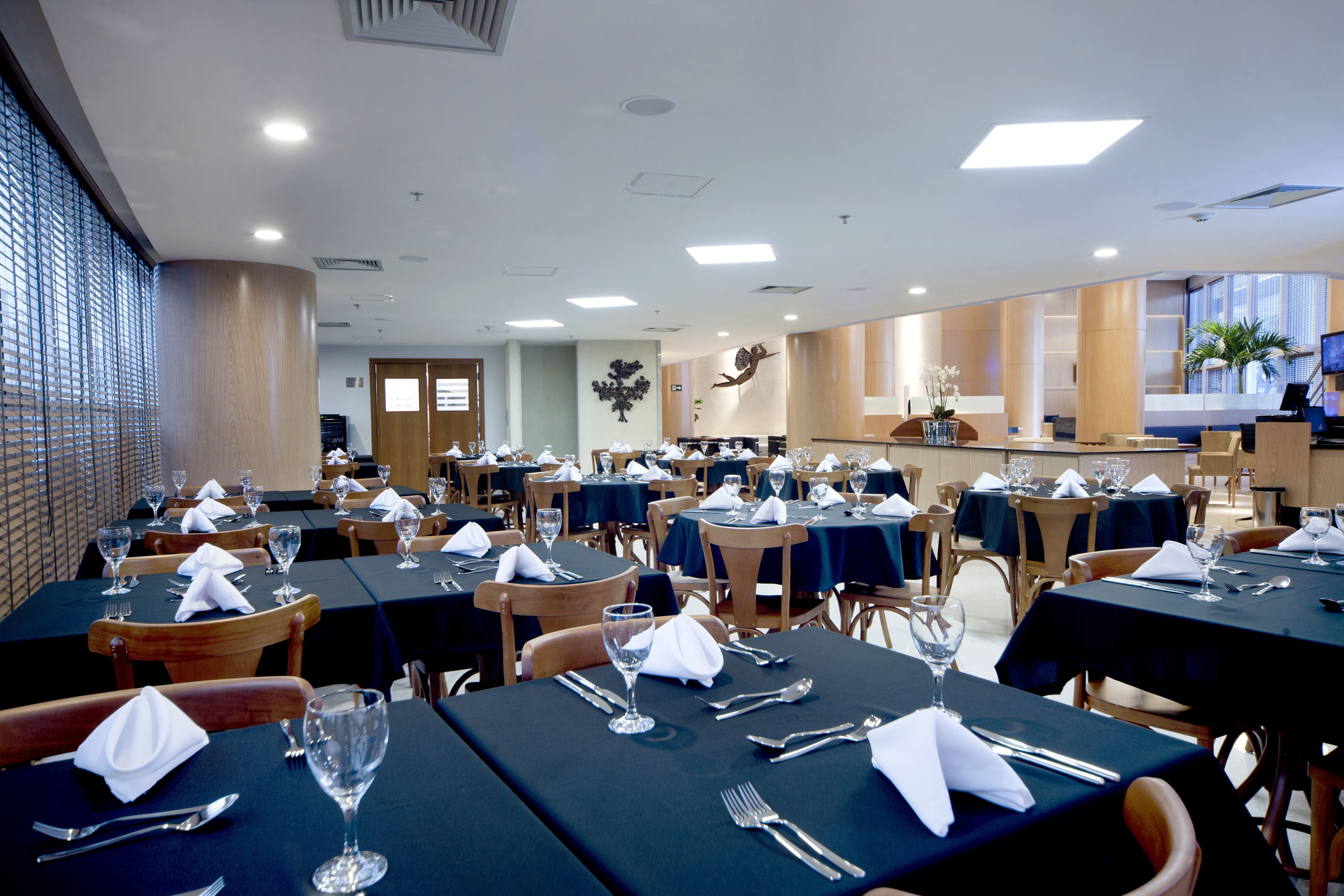 Un comedor espacioso con varias mesas dispuestas para los comensales, que presenta un diseño moderno con sillas de madera y manteles oscuros.