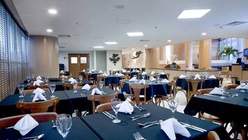 Un comedor espacioso con varias mesas dispuestas para los comensales, que presenta un diseño moderno con sillas de madera y manteles oscuros.