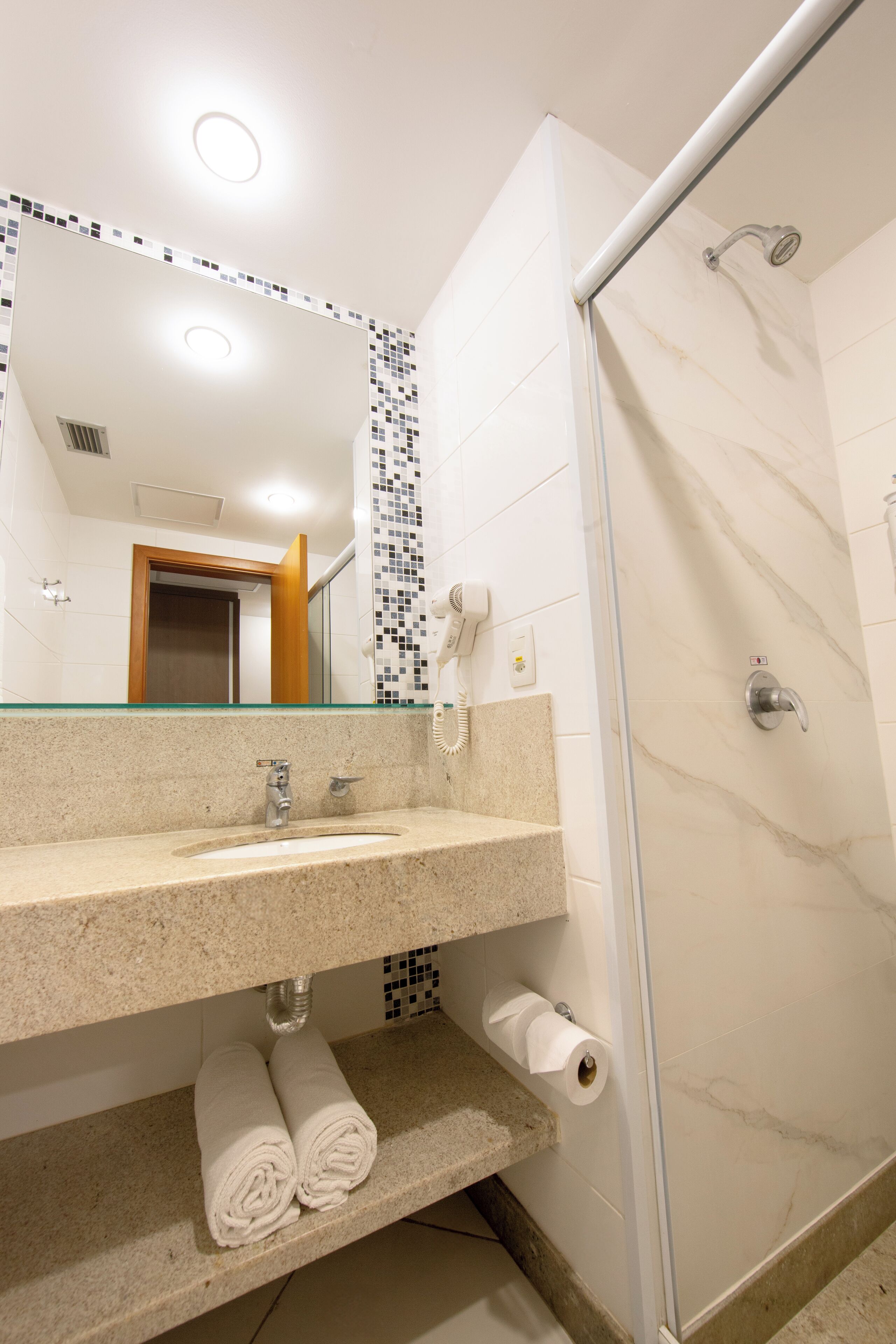 A bathroom with a glass shower enclosure, a sink with a towel rack, and a mirror with a mosaic backsplash.
