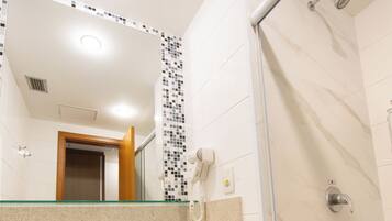A bathroom with a glass shower enclosure, a sink with a towel rack, and a mirror with a mosaic backsplash.