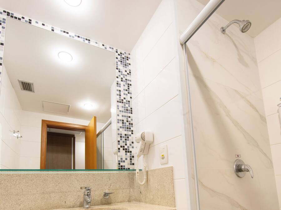 A bathroom with a glass shower enclosure, a sink with a towel rack, and a mirror with a mosaic backsplash.