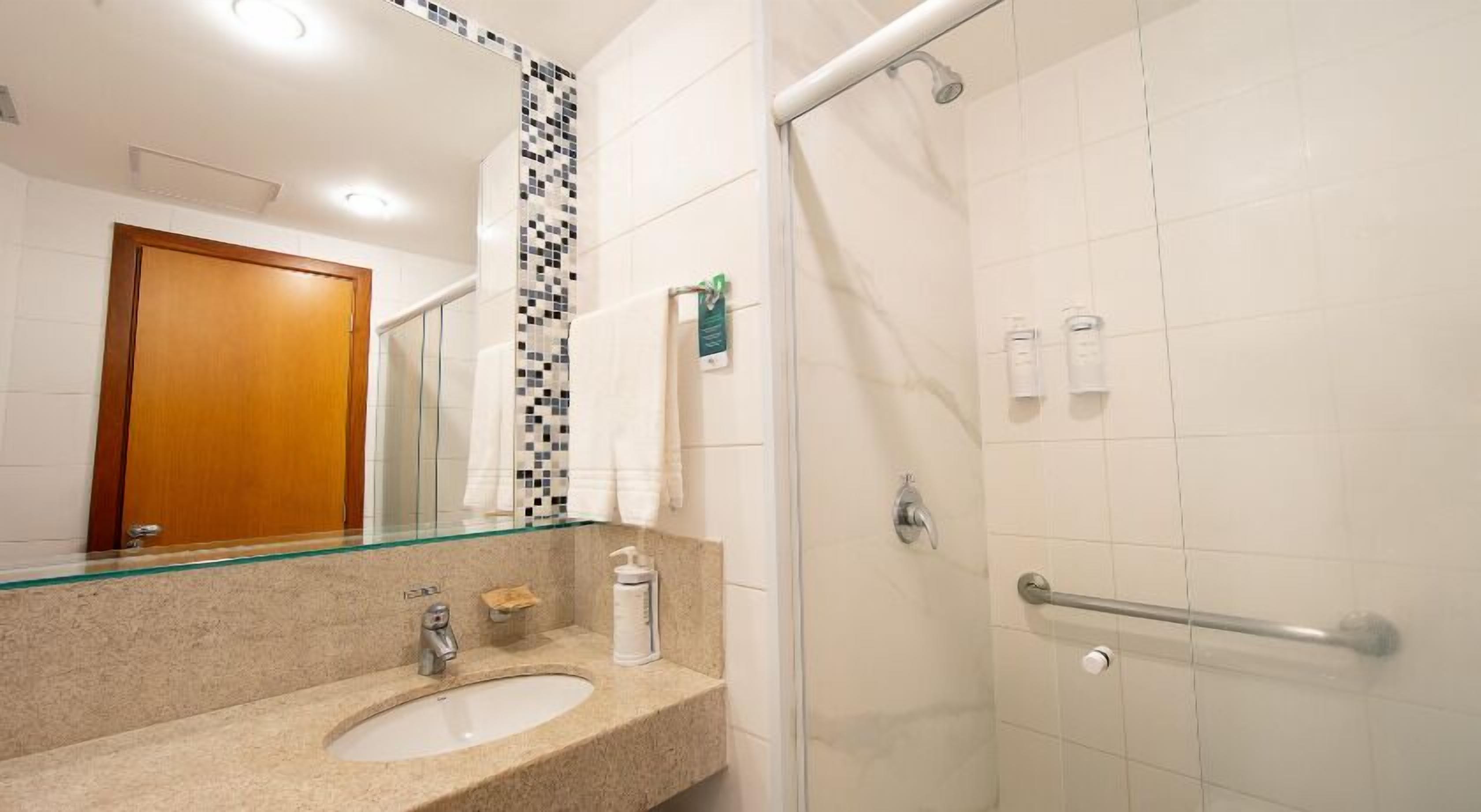 Un baño con lavamanos, espejo, ducha y barras de apoyo.