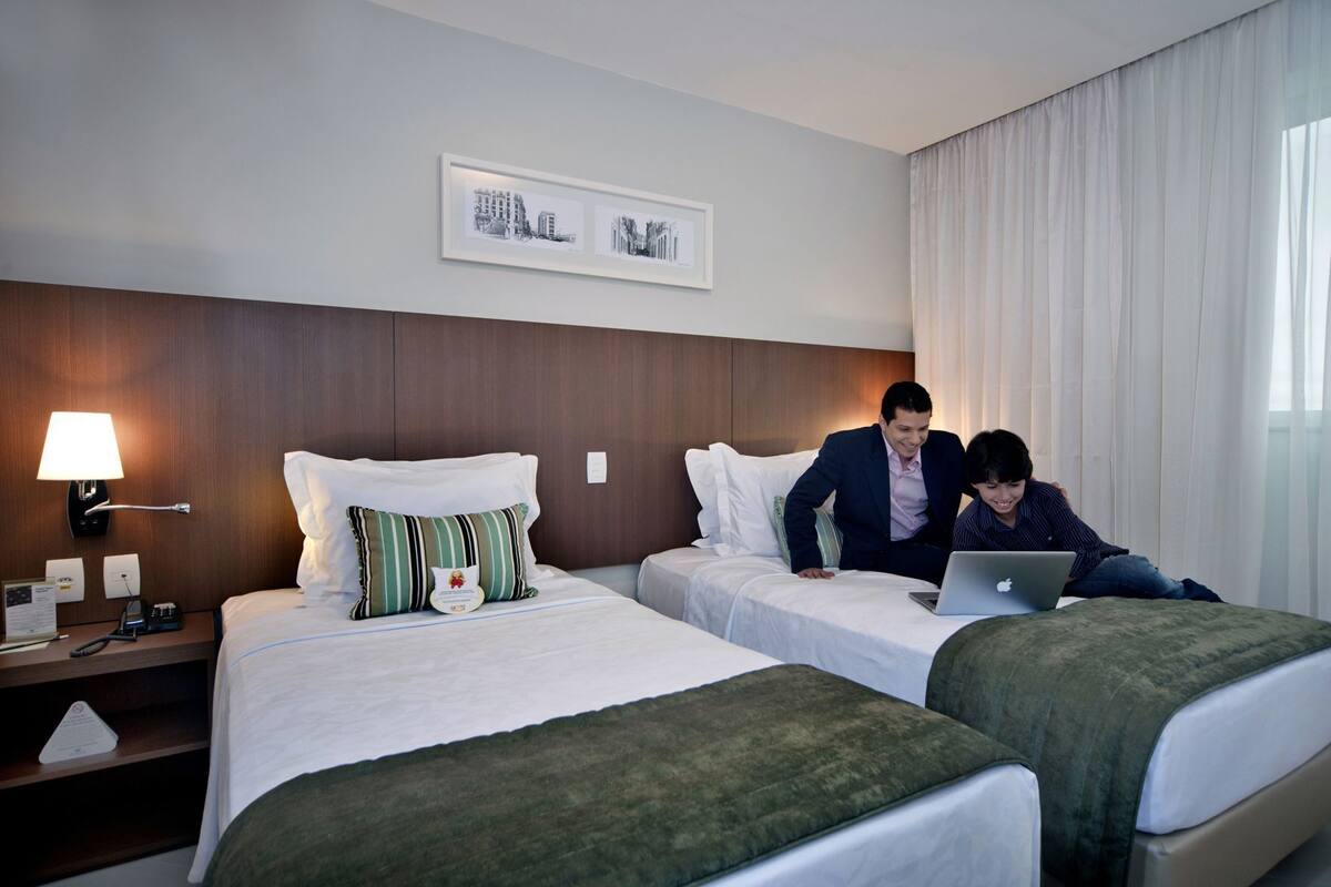 A hotel room with two beds, a desk, a lamp, and a framed picture on the wall.