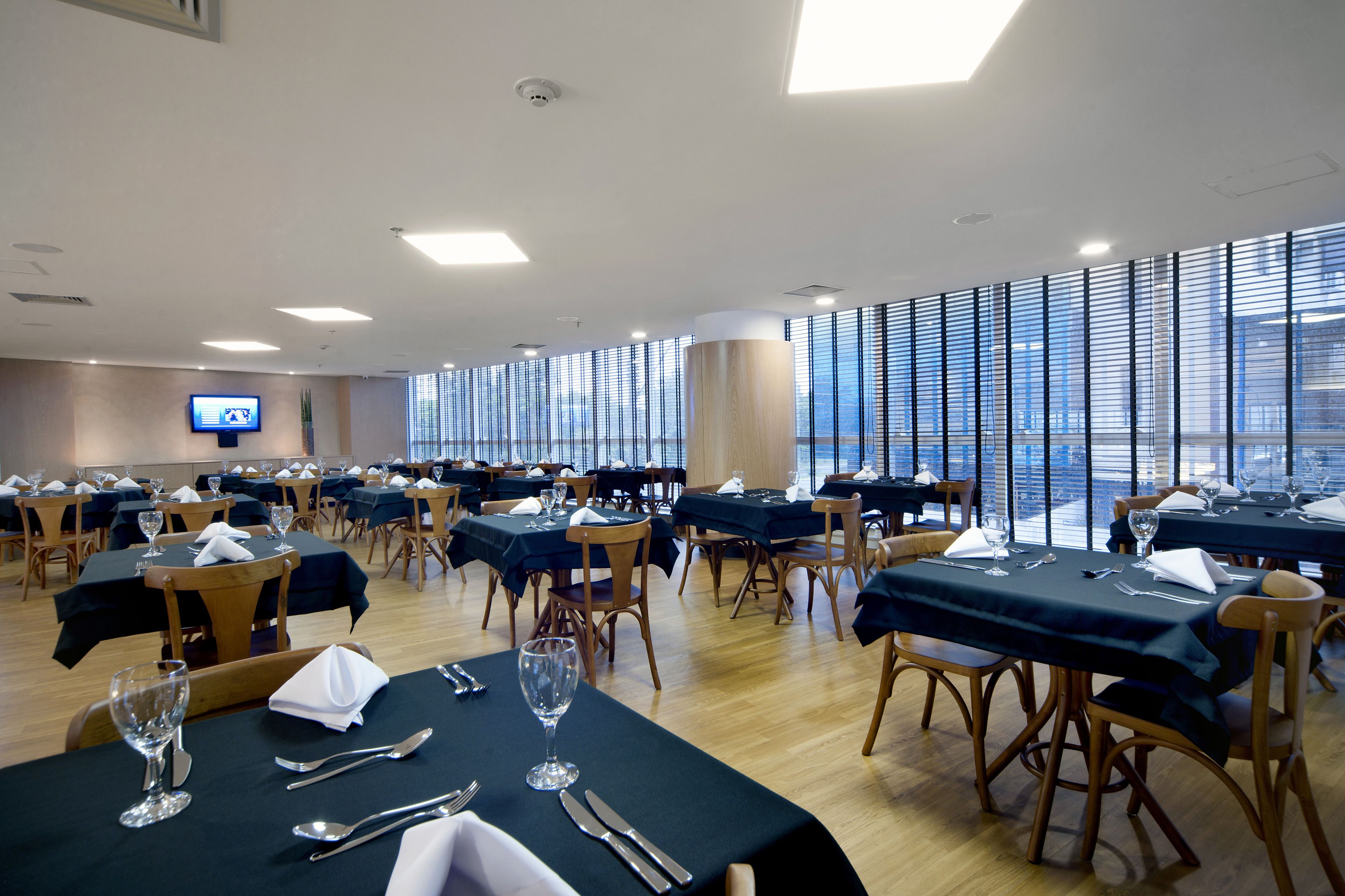 A conference room with multiple tables set for dining, equipped with chairs, tables, and a flat-screen TV on the wall.