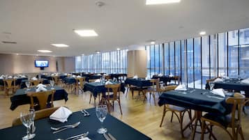 A conference room with multiple tables set for dining, equipped with chairs, tables, and a flat-screen TV on the wall.