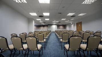 Un salón de conferencias con hileras de sillas color beige y alfombra azul.