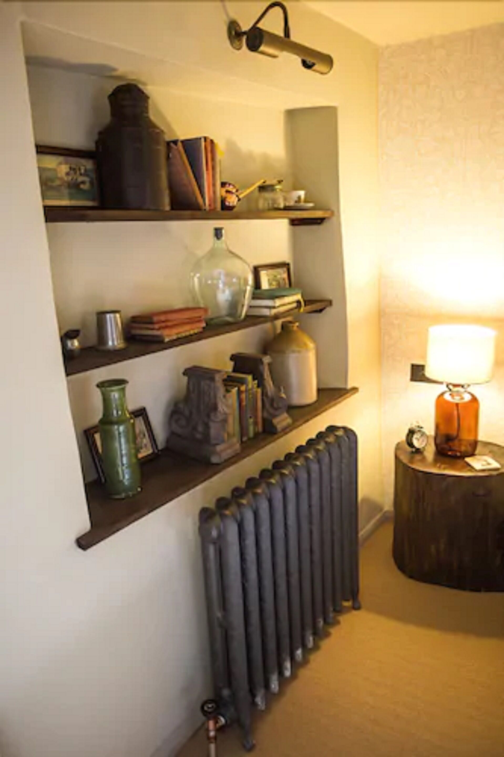 A room with a radiator, shelves with books and decorative items, and a lamp on a side table.