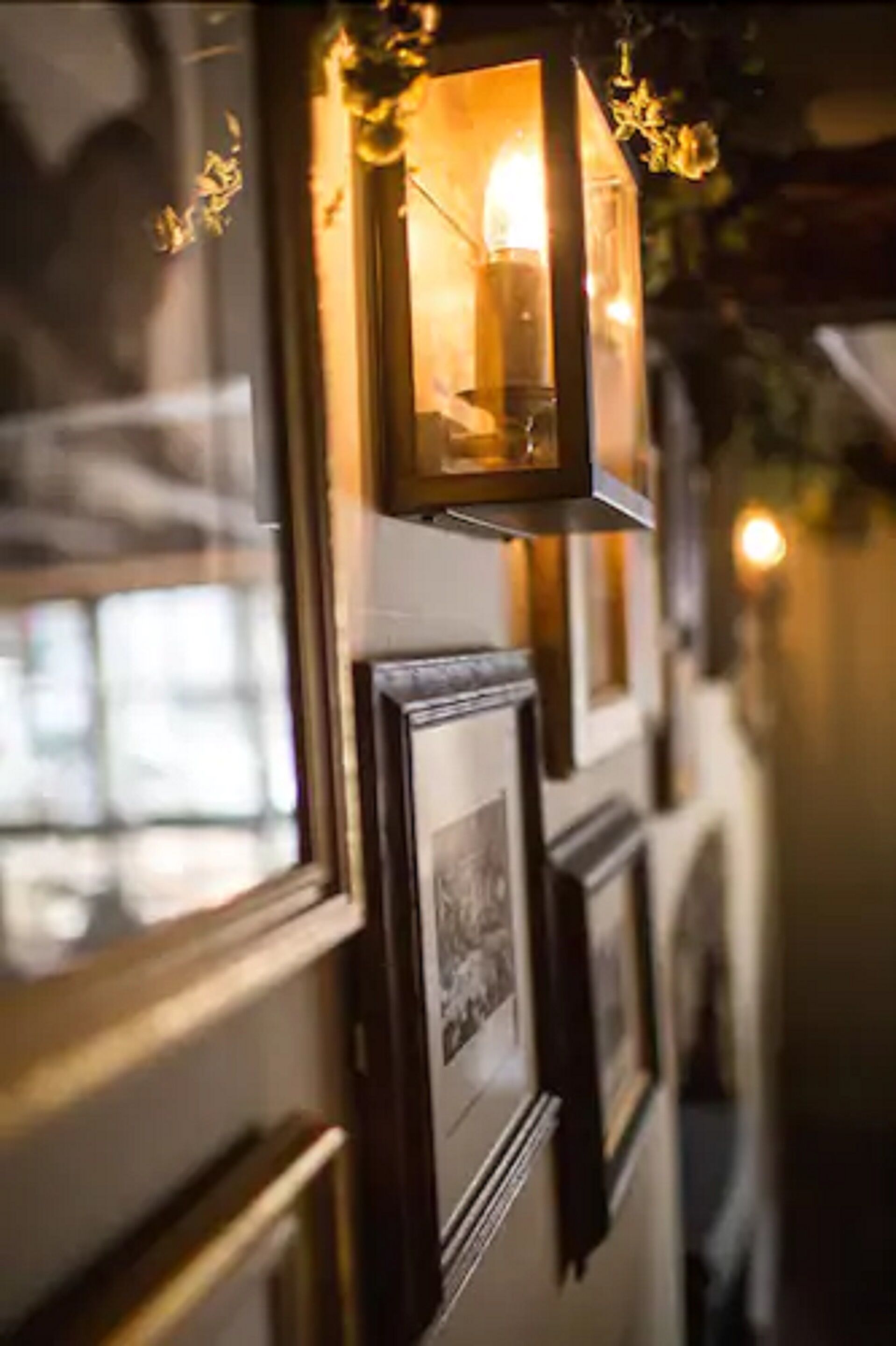 A corridor with framed pictures on the wall and a lit lantern hanging above.
