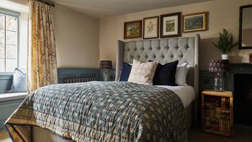 A bedroom with a large bed, a headboard, a window with curtains, a fireplace, and framed artwork on the wall.