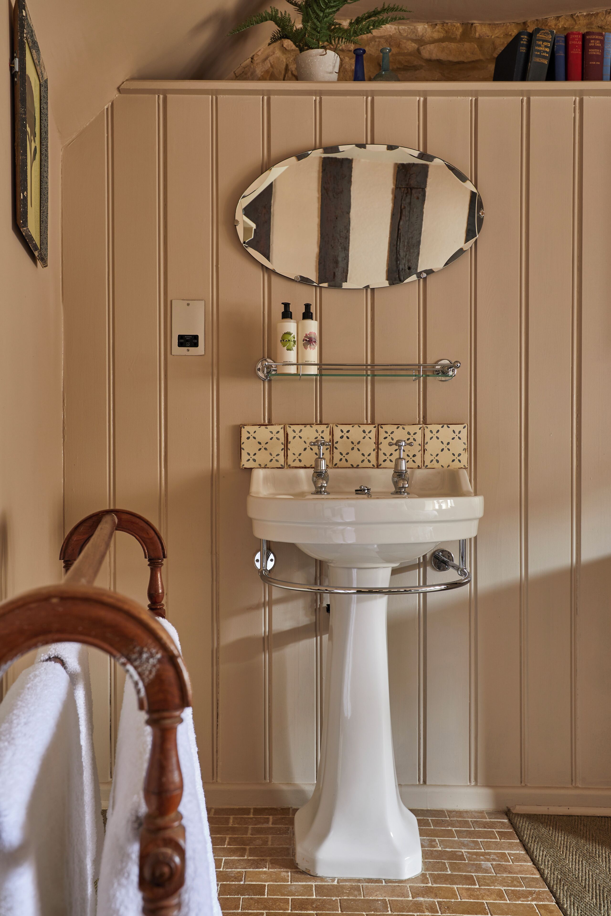A bathroom with a white pedestal sink, a mirror above it, and a shelf with toiletries.