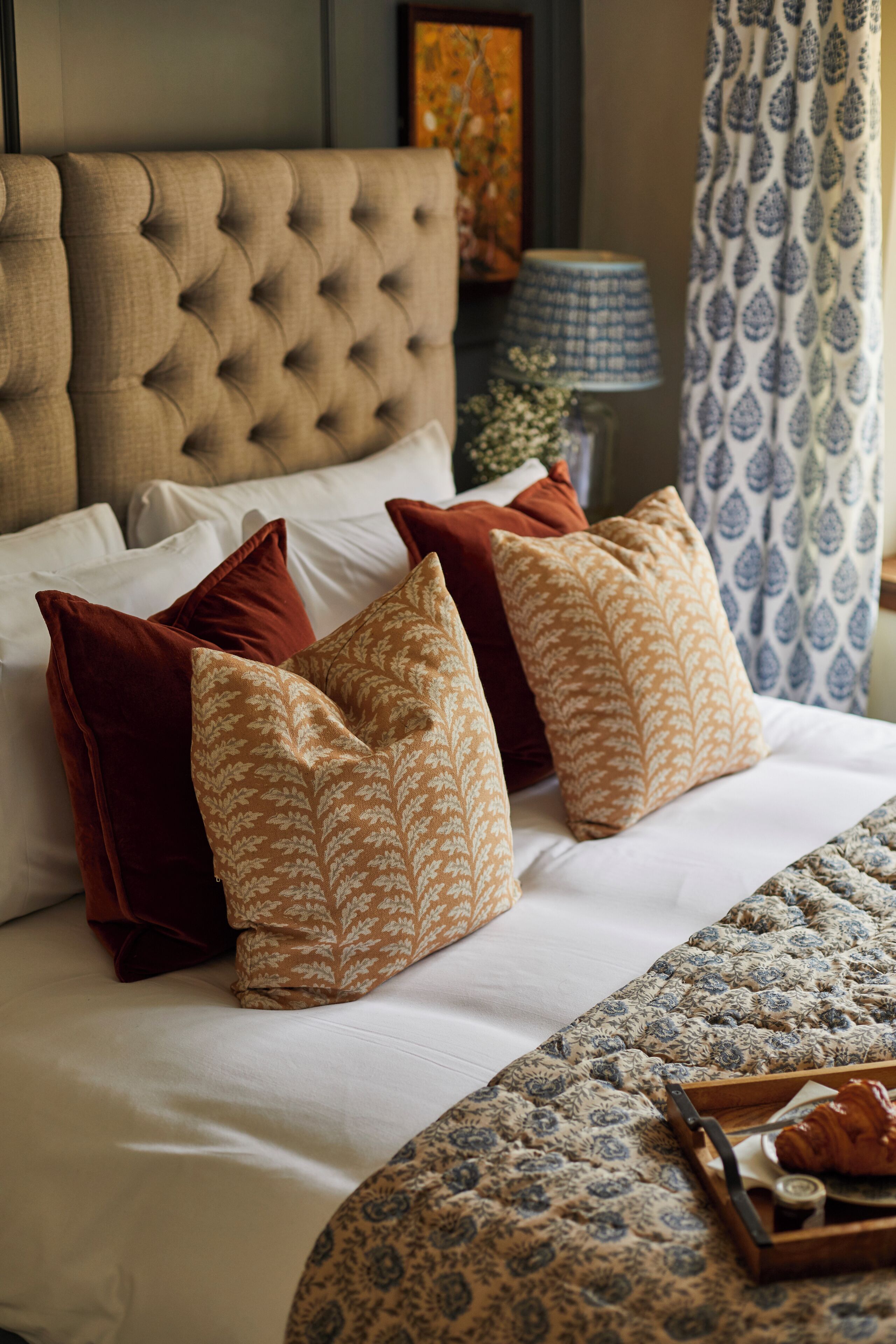 Una cama bien hecha con almohadas estampadas y una bandeja decorativa con un croissant.