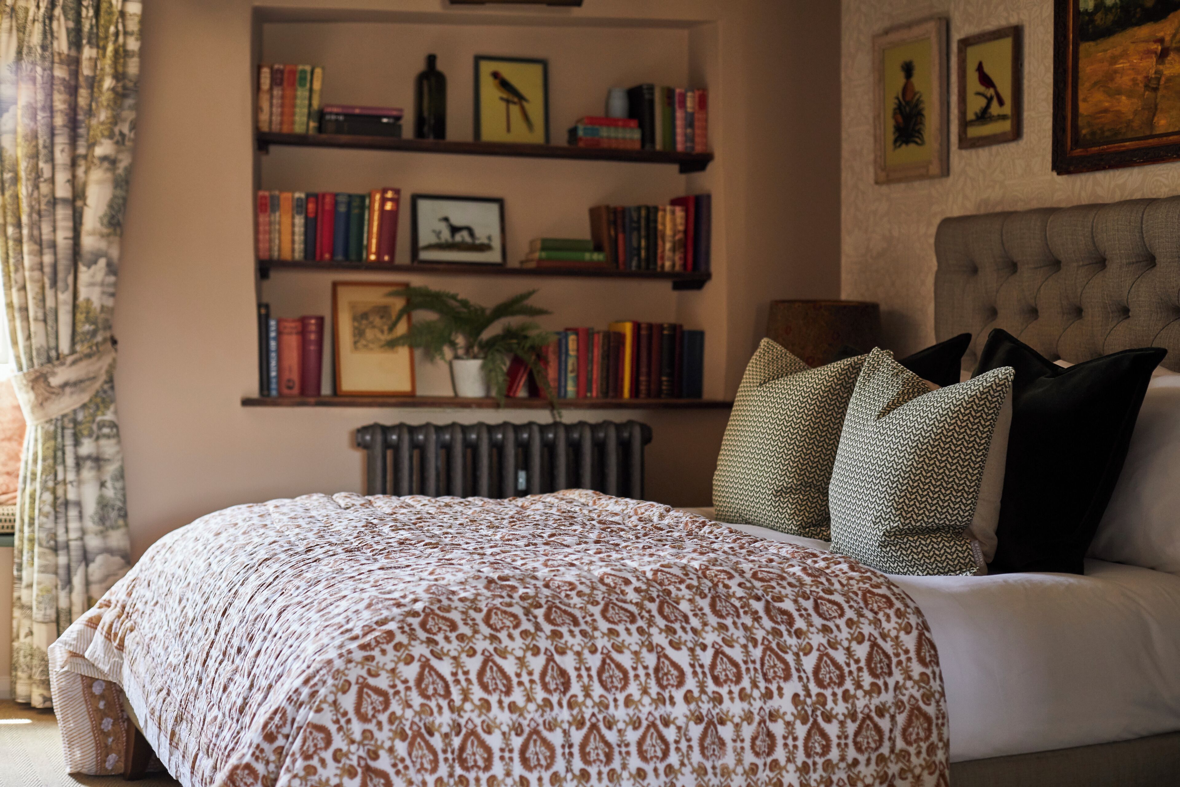 A bedroom with a large bed, a bookshelf, a radiator, and a window with curtains.